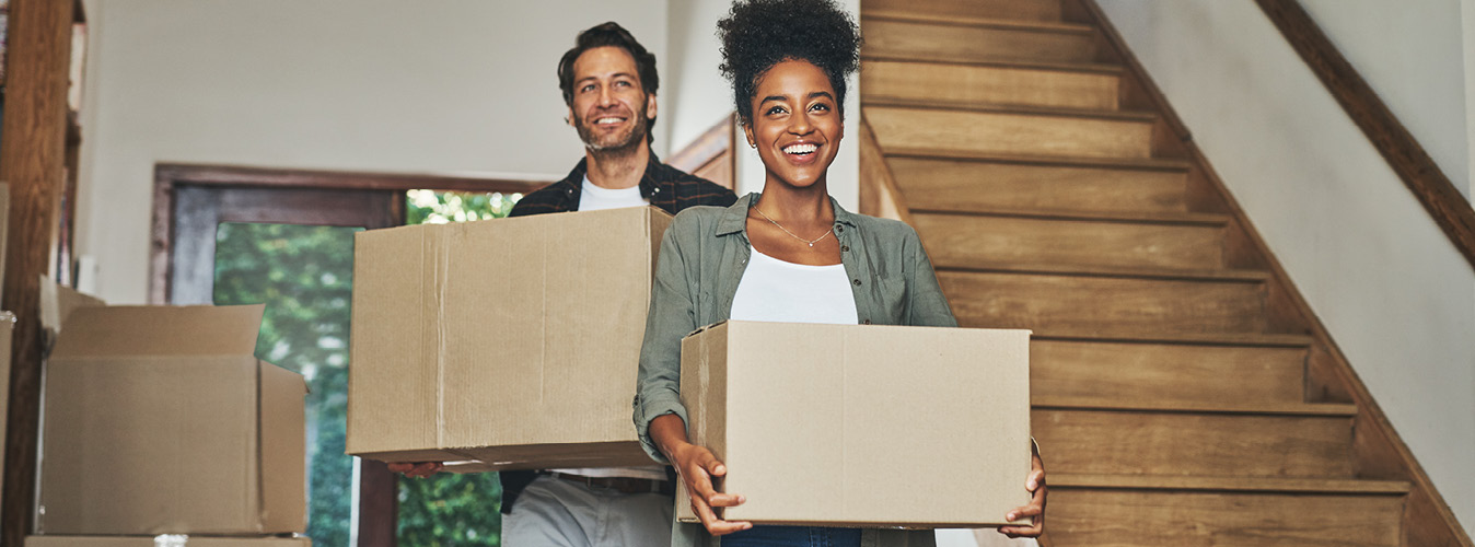 Happy couple, real estate and moving in new home with boxes for renovation, investment or relocation. Interracial man and woman owner carrying box for property rent, mortgage loan or move together
